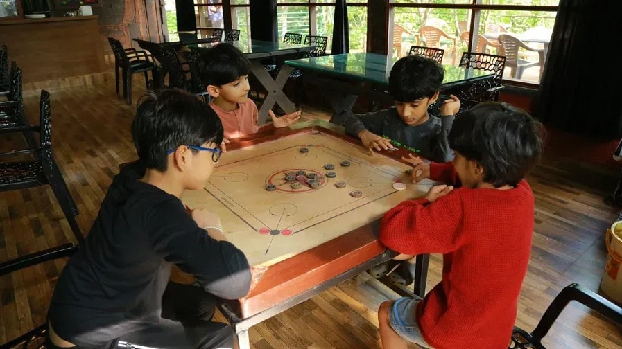 Children playing carrom board game indoors at Holistic Eco-Resort