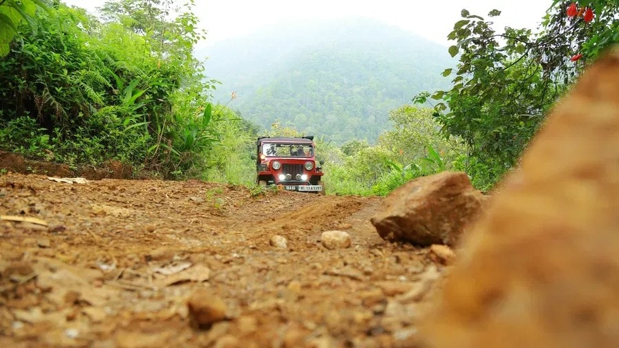 Red jeep climbing a rugged mountain trail through lush jungle at Holistic Eco-Resort