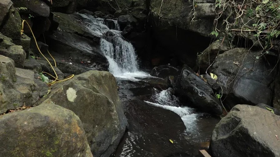 Private waterfall cascading over dark rocks in the jungle at Holistic Eco-Resort