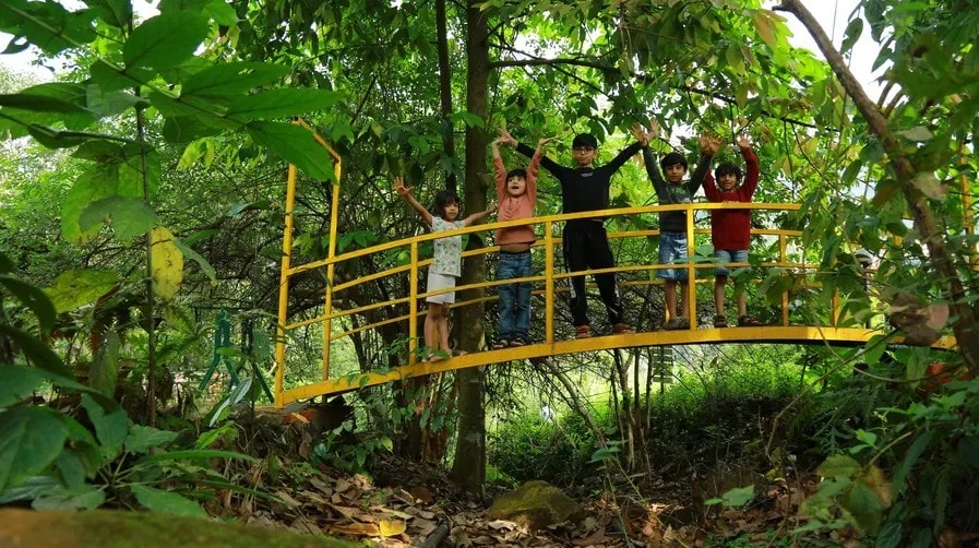 Children cheering on the yellow arched bridge in the jungle at Holistic Eco-Resort