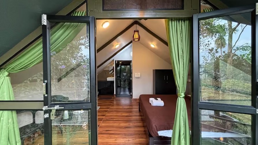 Interior of a forest-view room with vaulted ceiling, green curtains and wooden floor at Holistic Eco-Resort