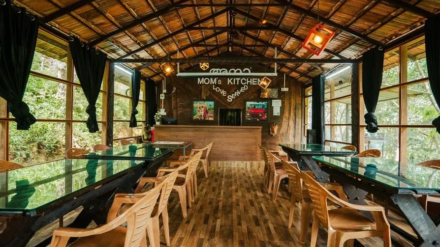 Interior of Mom's Kitchen with long glass-top tables and thatched roof surrounded by jungle